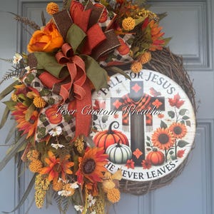 May include: A fall-themed wreath with sunflowers, pumpkins, and a decorative sign that reads "Fall for Jesus, He Never Leaves." The wreath features a variety of fall colors, including orange, brown, and green.