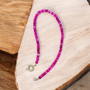 May include: A pink beaded necklace with a gold clasp. The beads are small and round, and the necklace is about 18 inches long.