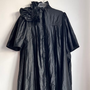 Puede incluir: Un vestido negro de manga corta con cuello de volantes y falda plisada.