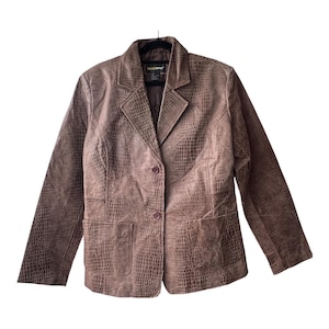 Può includere: Un blazer marrone con un motivo testurizzato in pelle di coccodrillo su tutta la superficie. Questa giacca a maniche lunghe presenta un bavero dentellato, due bottoni frontali per la chiusura e due grandi tasche applicate in vita. L'etichetta interna riporta la scritta Metrostyle.
