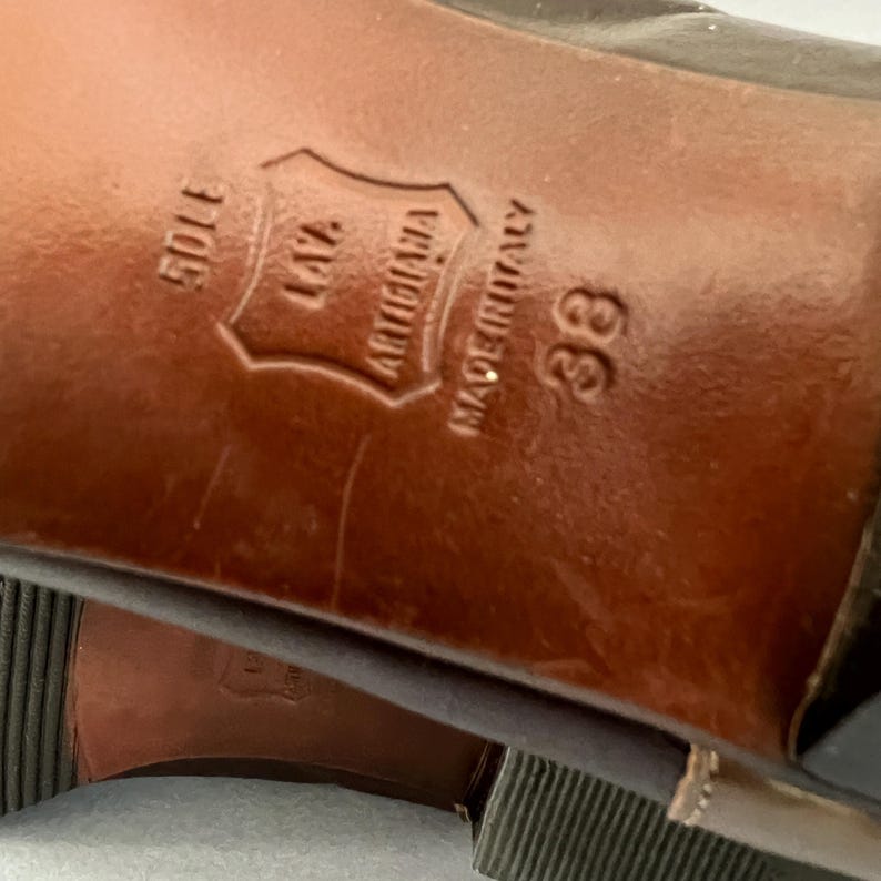 May include: The brown leather sole of a shoe featuring the embossed text VERO CUOIO, LAZ ARTIGIANA, MADE IN ITALY, and the size 38. The sole has a smooth, polished finish with visible light surface scratches and a dark brown heel section.