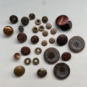 May include: A selection of antique buttons in diverse sizes, shapes, and hues. The metal buttons showcase elaborate designs, such as floral patterns, embossed details, and military emblems. Colours include gold, bronze, copper, and brown.