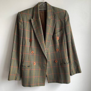 May include: A double-breasted blazer with a plaid pattern in shades of green, brown, and red. The blazer has four buttons and flap pockets.