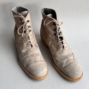 May include: A pair of light brown suede lace-up ankle boots with brogue detailing. The boots have a rounded toe and a lace-up closure.