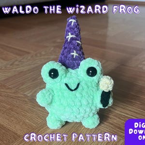 Op de afbeelding: Haakpatroon voor een groene kikker met een paarse tovenaarshoed en een witte bloem. Het patroon heet "Waldo the Wizard Frog".
