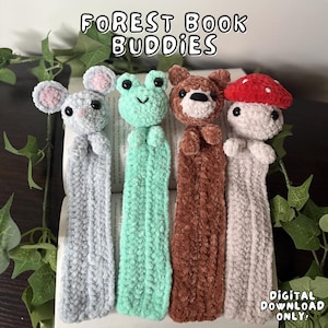 Può includere: Quattro segnalibri all'uncinetto fatti a mano a forma di creature della foresta: un topo, una rana, un orso e un fungo. I segnalibri sono in un libro, con il testo "FOREST BOOK BUDDIES" in alto. Le parole "DIGITAL DOWNLOAD ONLY" sono in basso.