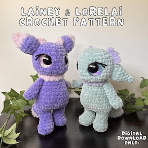 Pode incluir: Duas bonecas de crochê feitas à mão, uma roxa e outra verde-azulado, com olhos grandes e brilhantes e detalhes em rosa. As bonecas estão rotuladas como "Lainey & Lorelai Crochet Pattern" e "Digital Download Only."
