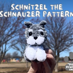 Könnte beinhalten: Ein graues und weißes gehäkeltes Miniatur-Schnauzer-Plüschtier. Das Spielzeug wird in einer Hand vor einem verschwommenen Hintergrund aus Bäumen und blauem Himmel gehalten. Der Text "Schnitzel the Schnauzer Pattern *Digital Download Only*" ist im Bild sichtbar.