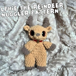 May include: A crocheted reindeer snuggle toy with large eyes and a red collar. The toy is lying on a fluffy white blanket. The text "Ralphie the Reindeer Snuggler Pattern" is written in black letters above the toy. The text "*Digital Download Only*" is written in black letters in the bottom right corner of the image.