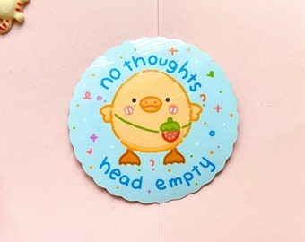 Puede incluir: Una pegatina azul claro con un pato de dibujos animados sosteniendo una fresa y el texto "no thoughts head empty". La imagen también incluye pequeños amuletos de gato y flores rosas sobre un fondo rosa.
