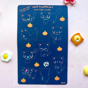 May include: A dark blue sticker sheet featuring black cat illustrations with orange pumpkins. Text includes "VOID PUMPKINS" and "Smol Tiger Studio". The sheet also has the text "find the voids in the void" and the code "SSO15".