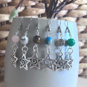 Op de afbeelding: Zes paar zilveren steroorbellen met verschillende gekleurde edelsteen kralen. De kralen zijn roze, wit, bruin, blauw, zilver en groen.