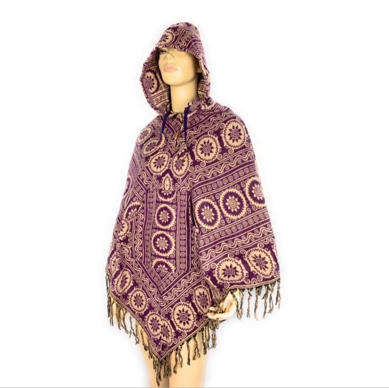K&ouml;nnte beinhalten: Lila und beigefarbener Kapuzenponcho mit geometrischem Muster und Fransenbesatz.