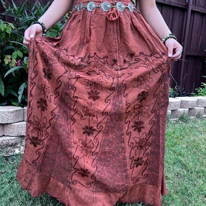 May include: A long, rust-colored skirt with a floral pattern and a ruffled hem. The skirt is made of a soft, flowing fabric and has a drawstring waist.