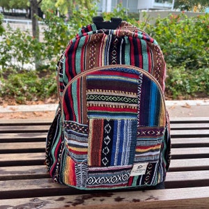 Può includere: Uno zaino intrecciato multicolore con un design a patchwork. Lo zaino ha una tiretta per la cerniera in pelle marrone e un piccolo cartellino in pelle marrone con il testo "Puzzle Stack" su di esso.