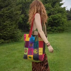 May include: A colorful patchwork tote bag with a peace sign, Om symbol, and other symbols. The bag has a ruffled edge and is made of different fabrics.