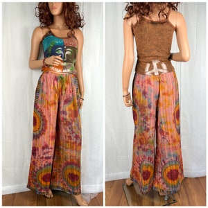 Puede incluir: Un par de pantalones anchos de tie-dye con un signo de paz en la espalda. Los pantalones est&aacute;n hechos de una tela suave y fluida y tienen un ajuste holgado. Los pantalones son una mezcla de colores rosa, naranja y amarillo.