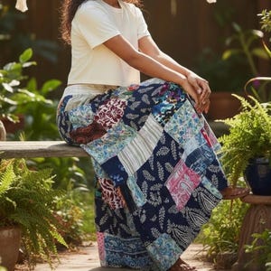 May include: A short-sleeved white crew neck t-shirt paired with a long, flowing patchwork skirt. The skirt features a variety of blue, pink, and white fabric panels with diverse floral, paisley, and leaf patterns, finished with an elastic waistband.