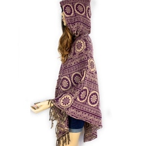 K&ouml;nnte beinhalten: Lila und beigefarbener Kapuzenponcho mit geometrischem Muster und Fransenbesatz.