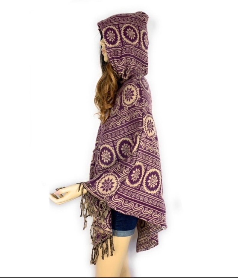 K&ouml;nnte beinhalten: Lila und beigefarbener Kapuzenponcho mit geometrischem Muster und Fransenbesatz.