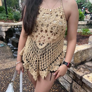 May include: A beige crochet halter top with a floral pattern. The top is loose fitting and has a scalloped hem.
