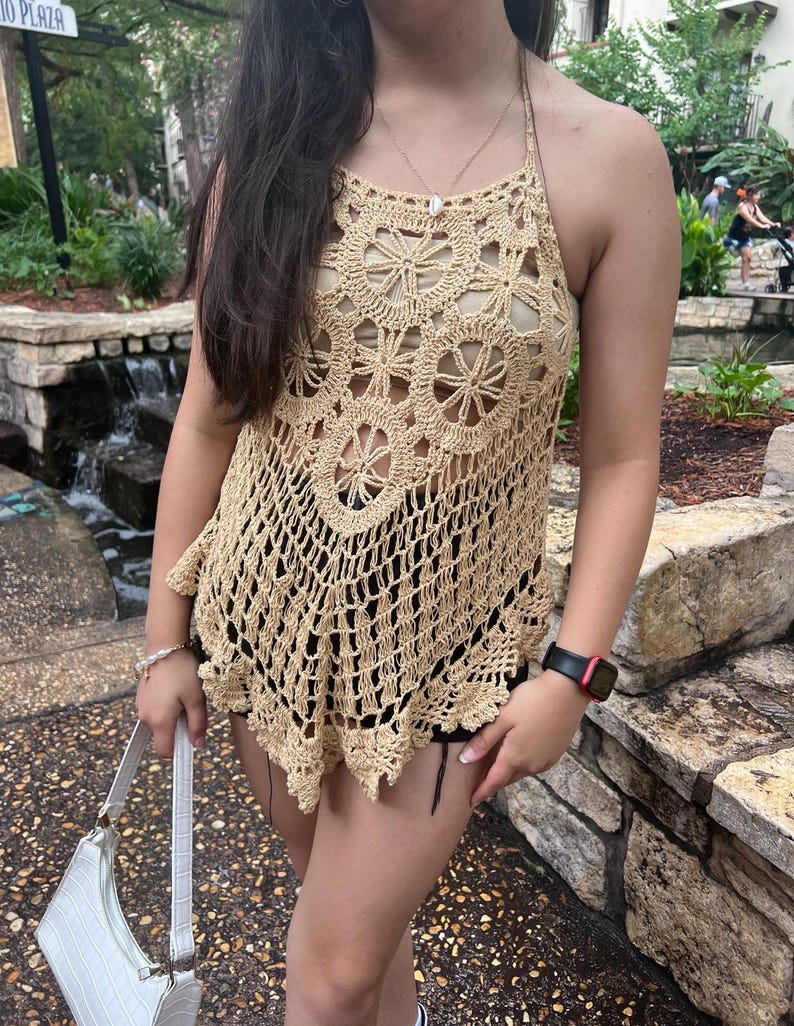 May include: A beige crochet halter top with a floral pattern. The top is loose fitting and has a scalloped hem.