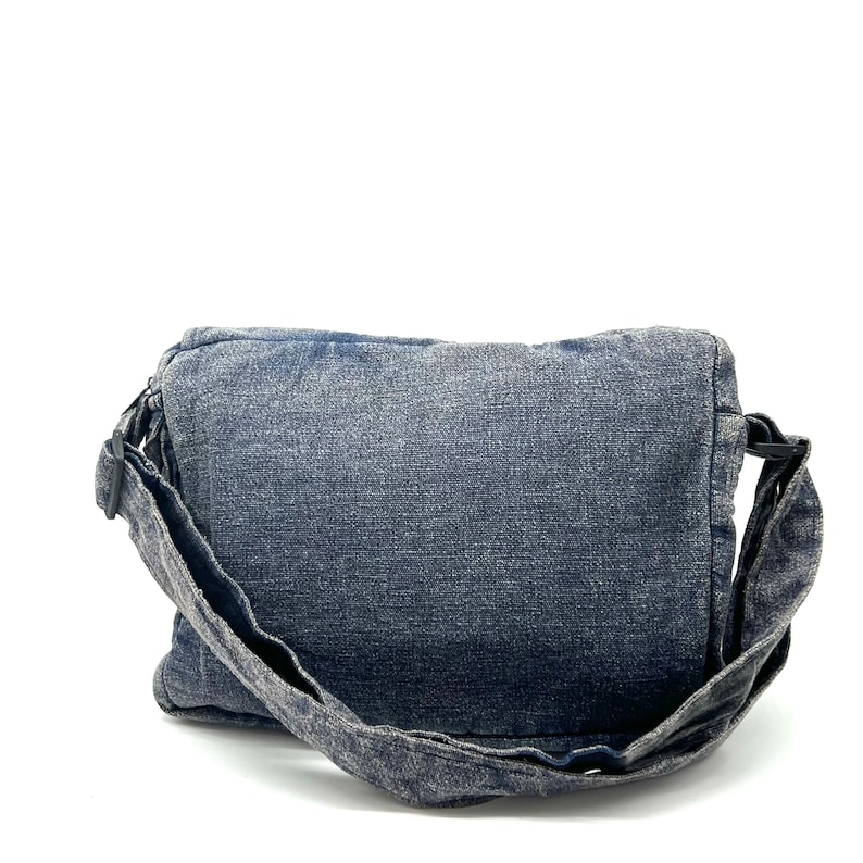 Może przedstawiać: Niebieska torba na ramię z denimu z długim, regulowanym paskiem. Torba ma klapkę zamykaną na zatrzask i prosty design.