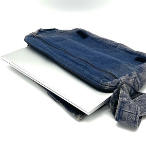 Może przedstawiać: Niebieska torba na laptopa z denimu z zamkiem błyskawicznym i paskiem na ramię. Torba jest otwarta, a w środku znajduje się srebrny laptop.