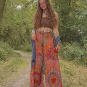 Puede incluir: Una mujer con un top marr&oacute;n corto, un cintur&oacute;n de cadena plateada con abalorios y pantalones tie-dye. Est&aacute; de pie en un entorno de bosque.