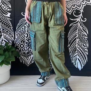 May include: Green cargo pants with blue and white patterned trim around the waist and legs. The pants have large pockets on the sides.