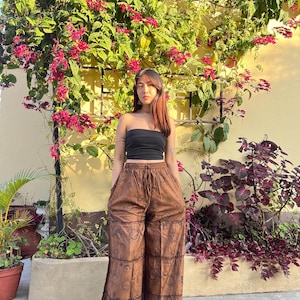 May include: A woman wearing a black strapless top and brown printed wide-leg pants with a high waist. The pants have a tiered design and are decorated with a pattern of suns and moons.