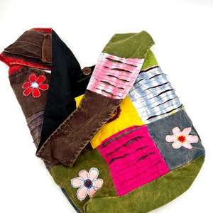 Puede incluir: Un bolso tote de patchwork con una correa marrón. El bolso está hecho de diferentes telas de colores, incluyendo verde, azul, rosa, amarillo y marrón. El bolso tiene un diseño floral con flores bordadas en rosa, rojo y azul.