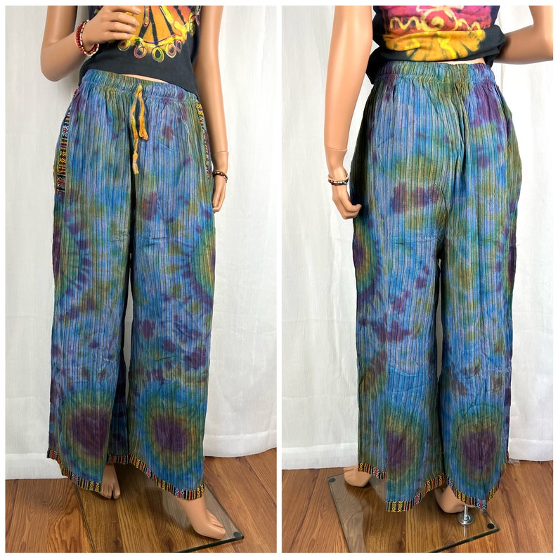 Puede incluir: Pantalones anchos de tie-dye con un patr&oacute;n a rayas en tonos azules, verdes y morados. Los pantalones tienen una cintura con cord&oacute;n y un ribete colorido a lo largo del dobladillo inferior.