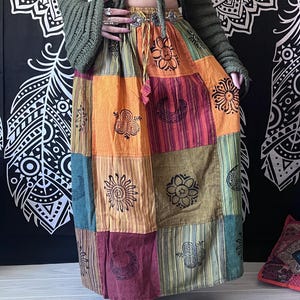 Puede incluir: Una falda larga de retazos multicolor con una variedad de dise&ntilde;os impresos. La falda est&aacute; hecha de algod&oacute;n y tiene un corte holgado. La falda es una mezcla vibrante de naranja, rojo, verde y marr&oacute;n.