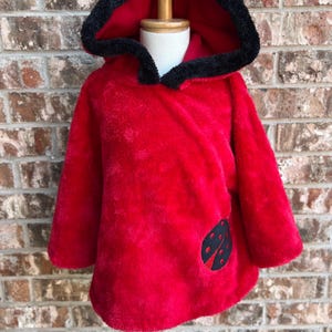 May include: Red hooded fleece poncho with a black trim and a ladybug applique.