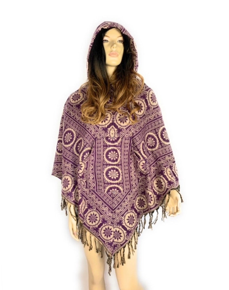 K&ouml;nnte beinhalten: Lilafarbener Kapuzenponcho mit geometrischem Muster in Beige. Der Poncho hat Fransen an den R&auml;ndern.