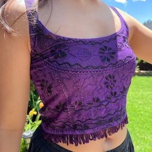 May include: Purple crop top with black embroidery and fringe trim. The top is made of a soft, flowing fabric and has a relaxed fit.