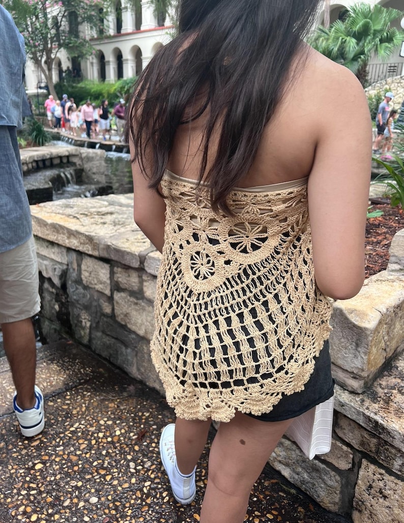 May include: A beige crochet top with a scalloped hem. The top is sleeveless and has a loose, flowy fit.