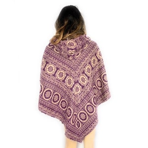 K&ouml;nnte beinhalten: Lilafarbener Kapuzenponcho mit einem cremefarbenen und lilafarbenen geometrischen Muster. Das Muster zeigt ein sich wiederholendes Design aus Kreisen und Spiralen.