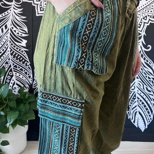 May include: Green cargo pants with blue and black patterned pockets. The pants have a drawstring waist and a relaxed fit.