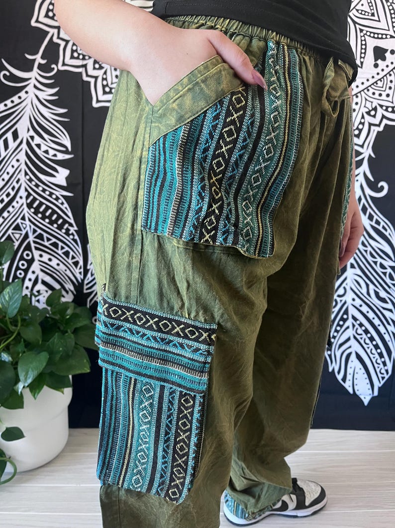 May include: Green cargo pants with blue and black patterned pockets. The pants have a drawstring waist and a relaxed fit.