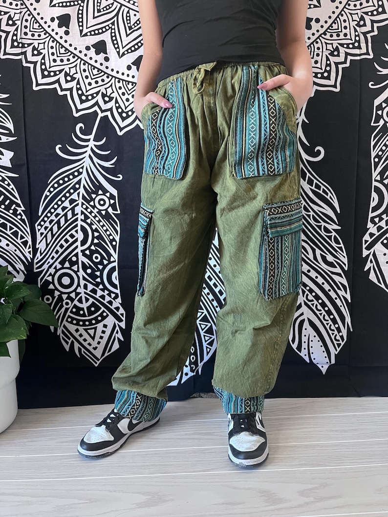 May include: Green cargo pants with blue and black patterned fabric panels. The pants have a drawstring waist and multiple pockets.