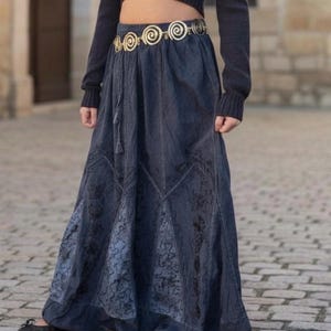 May include: A long, dark blue skirt with a floral pattern and a decorative gold belt. The skirt has a flowing design and is paired with a dark top. The belt features a spiral design.