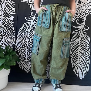 May include: Green cargo pants with blue and white patterned fabric accents on the pockets and cuffs. The pants have a drawstring waist and are worn with black sneakers.