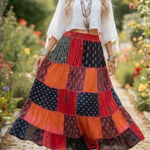 Puede incluir: Una falda larga hasta los tobillos de estilo patchwork que presenta una mezcla vibrante de paneles de tela rojos, naranjas y negros con diversos patrones geométricos y florales. La falda tiene una cintura elástica con cordón.