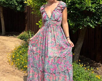 May include: A long, flowing dress with a paisley pattern in pink and teal. The dress features a V-neckline, ruffled cap sleeves, and a tiered skirt. The dress is made of a lightweight fabric, perfect for warm weather.