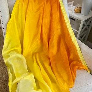 May include: A yellow and orange ombre silk scarf draped over a white armchair. The scarf has a light yellow border.