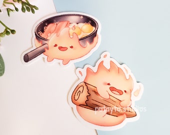 Op de afbeelding: Twee cartoon-vuur-stickers. Eén sticker toont een vuur dat een pan met eieren en spek vasthoudt. De andere sticker toont een vuur dat een houtblok vasthoudt. Beide stickers hebben een witte achtergrond.