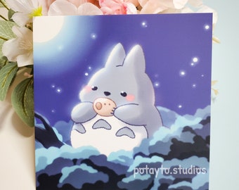 Puede incluir: Una linda ilustración de dibujos animados de un personaje Totoro gris y blanco sosteniendo un pequeño objeto marrón en sus patas. El fondo es azul oscuro con estrellas blancas y una gran luna blanca.
