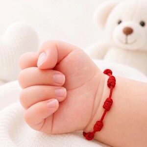 May include: A bright red cord bracelet featuring a series of small, evenly spaced decorative knots. The bracelet is worn around a wrist, showcasing the vibrant color and the intricate, textured knotting pattern of the cord material.
